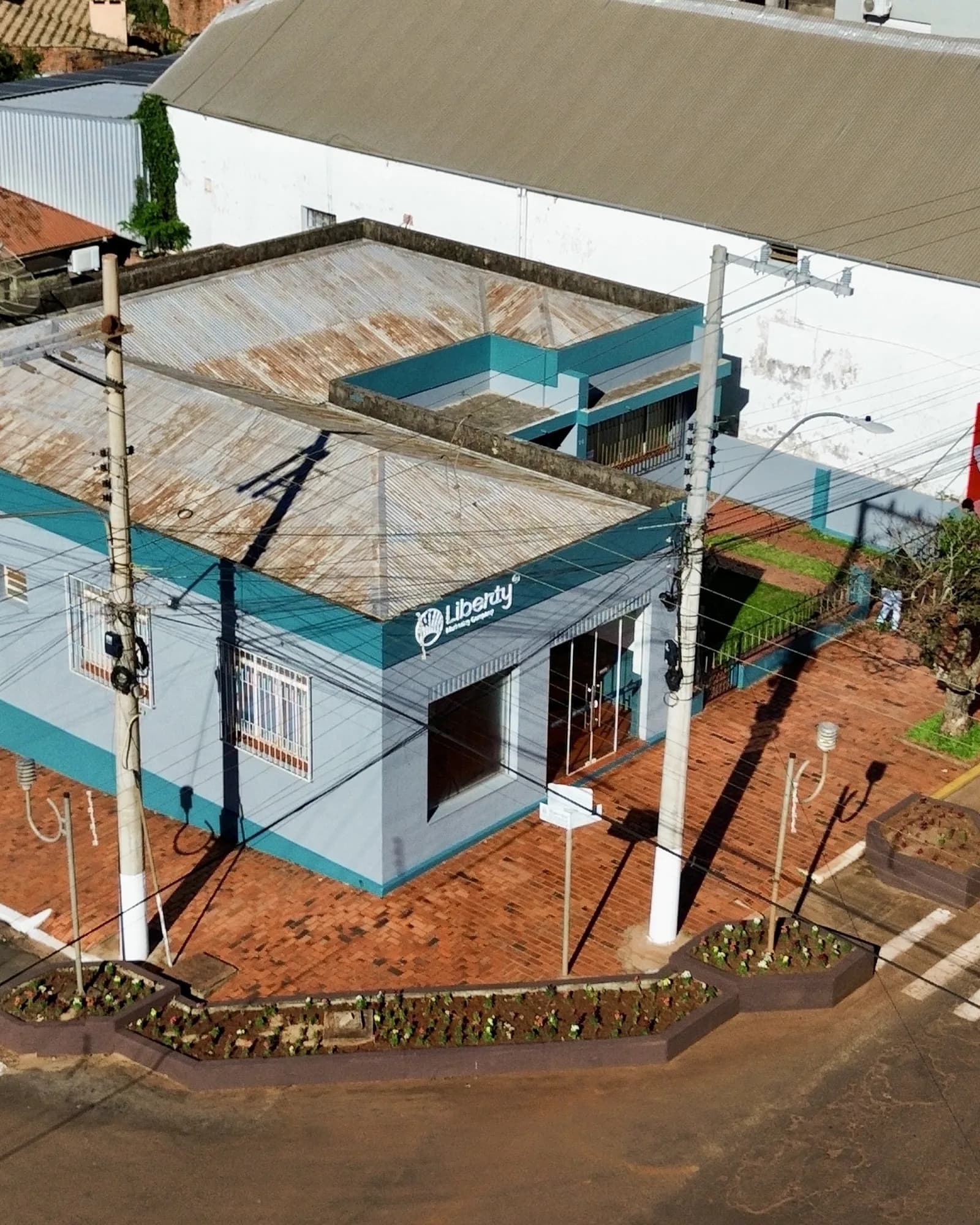 Vista aérea mais aberta do escritório da Liberty na esquina movimentada, com carros estacionados e faixa de pedestre