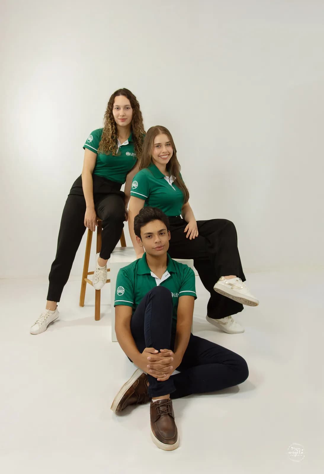 Trio do time Liberty de polo verde em ensaio de estúdio com fundo claro, duas pessoas atrás e uma sentada à frente